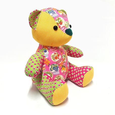 Kleurige knuffelbeer van stof met verschillende patronen en vrolijke kleuren.